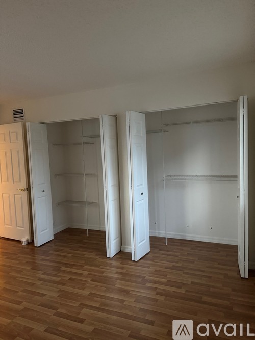 A room with white walls and wooden flooring, with a door on the left and two closets with white doors.