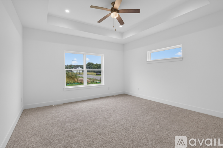 A room with a ceiling fan and a window showing a view of a house and trees.