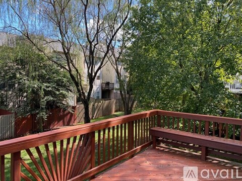 A wooden deck with a bench and trees in the background.