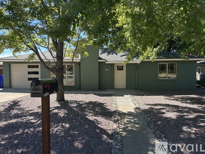A tree is in front of a green house with a mailbox on the left.