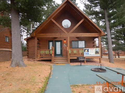 A wooden cabin with a green door and windows, surrounded by trees.