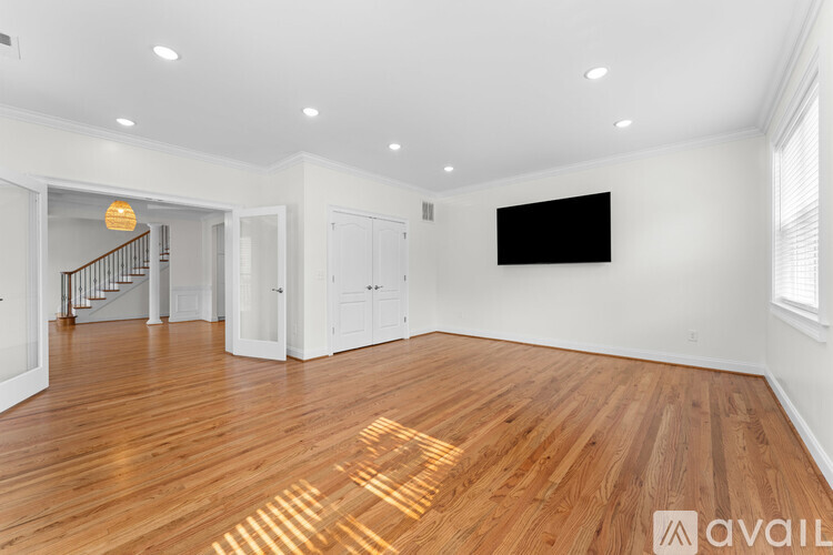 A spacious room with wooden floors and a staircase in the background.