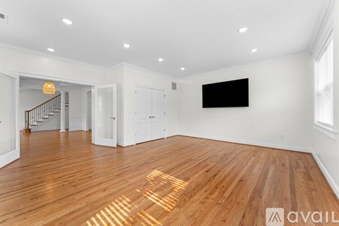 A spacious room with wooden floors and a staircase in the background.