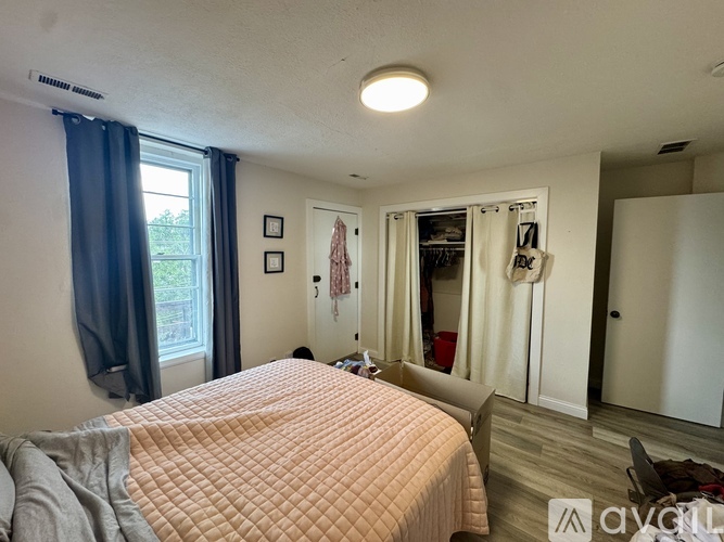 A bedroom with a bed, a window with curtains, and a closet with clothes hanging.