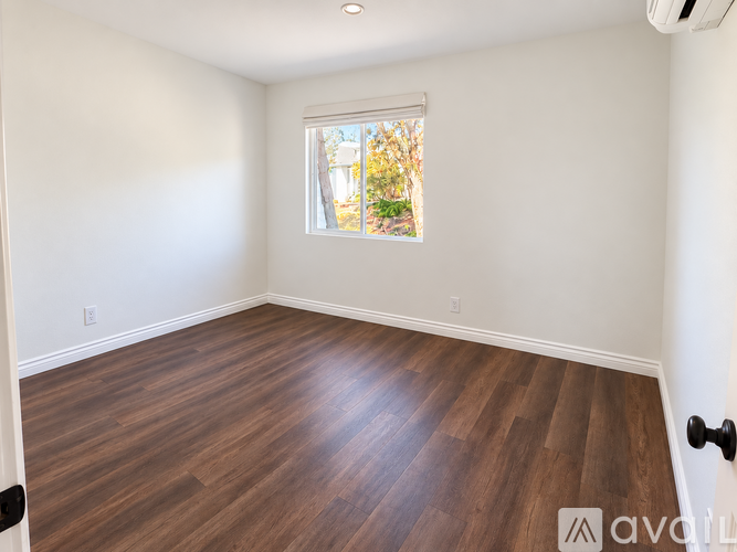 A room with wooden flooring and a window showing trees outside.