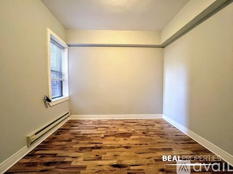A room with wooden flooring and a window on the left side.