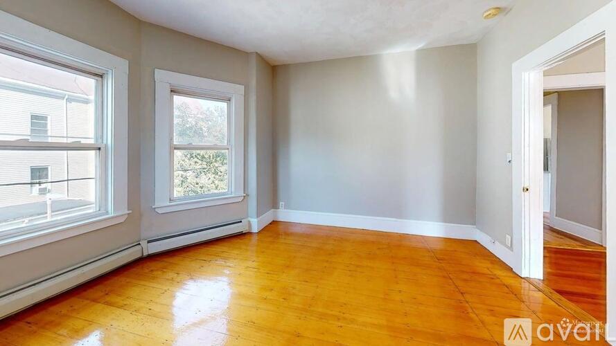 A room with wooden floors and white walls, with two windows and a door.