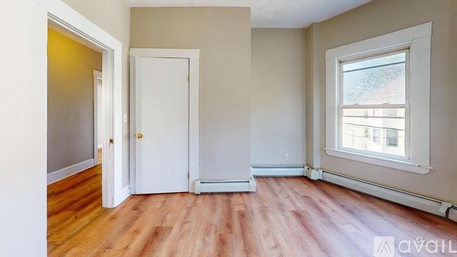 A room with a wooden floor, a white door, and a window with a view of a building outside.