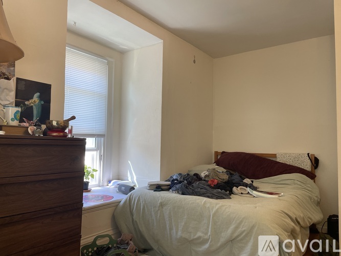 A messy bedroom with a bed, dresser, and window.