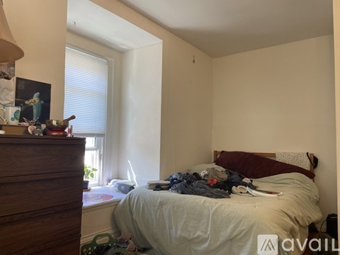 A messy bedroom with a bed, dresser, and window.