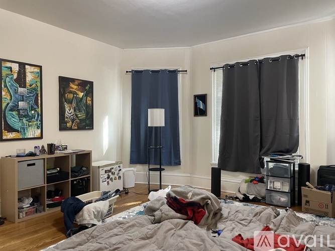 A messy bedroom with a bed in the center and a bookshelf to the left.