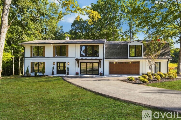 A white house with a brown garage door is surrounded by greenery.