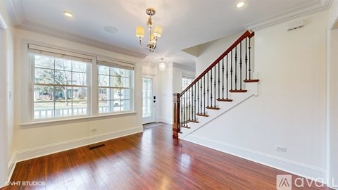 A spacious room with a wooden floor, a staircase with a black railing, and a chandelier hanging from the ceiling.