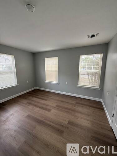 A room with wooden flooring and two windows.