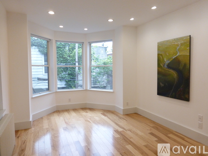 A room with a large painting on the wall and a view of trees through the windows.