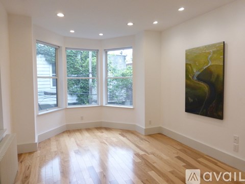 A room with a large painting on the wall and a view of trees through the windows.