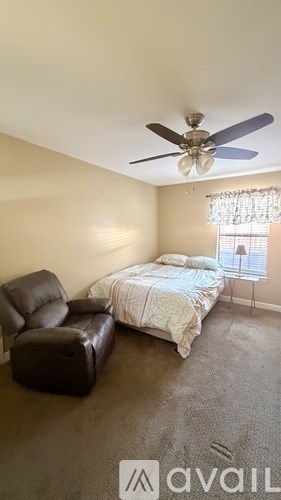 A bedroom with a bed, a chair, and a ceiling fan.