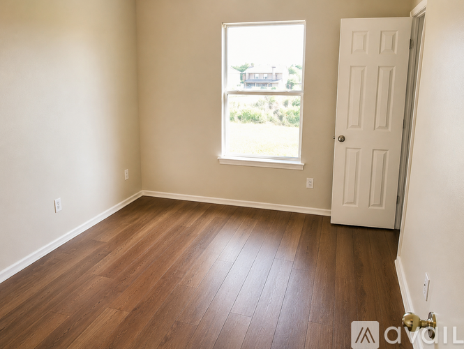 A room with a white door and a window with a view of a house across the street.