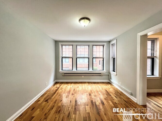 A room with wooden floors and a window with a view of a brick building.