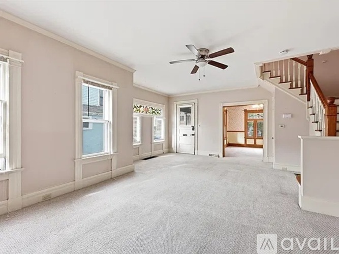 A spacious room with a fan and a staircase.