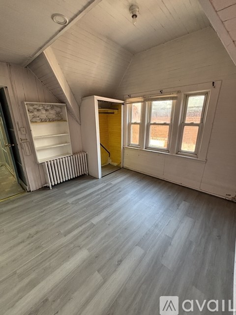 A room with wooden flooring and a window with a view of a brick wall.