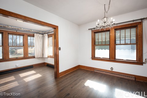 A room with a chandelier, wooden floors, and a window with a view of trees outside.