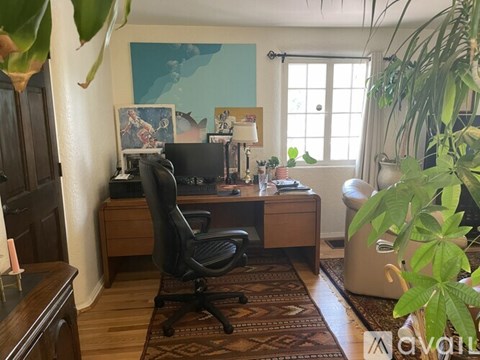 A room with a desk, chair, and a potted plant.