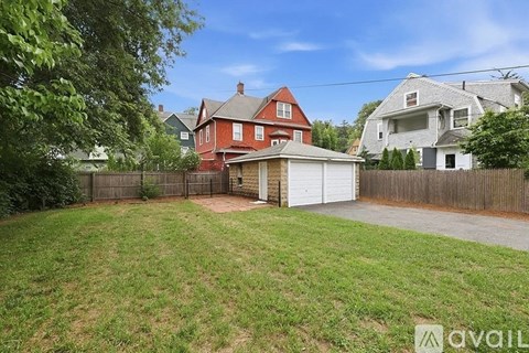 A red house with a white garage door is surrounded by a fence and green grass.