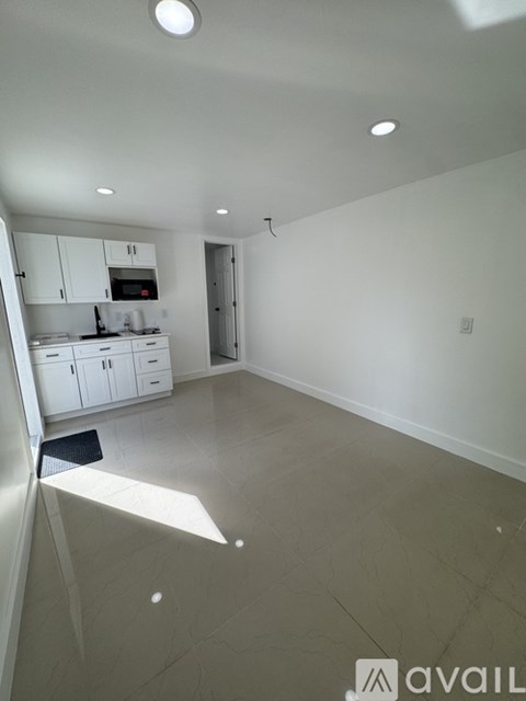 A spacious kitchen and living room with white cabinetry and a black mat on the floor.