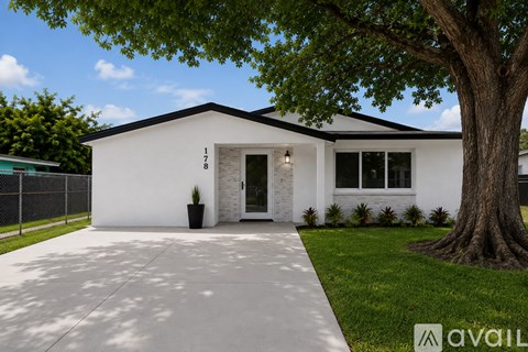 A white house with a black fence and a tree in front.