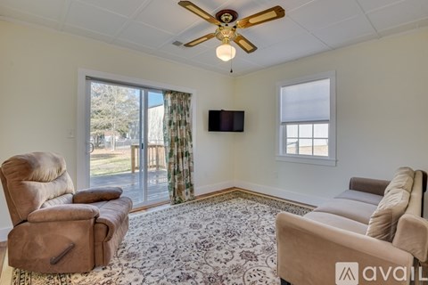 A living room with a beige sofa, armchair, and rug with a ceiling fan and sliding glass doors.
