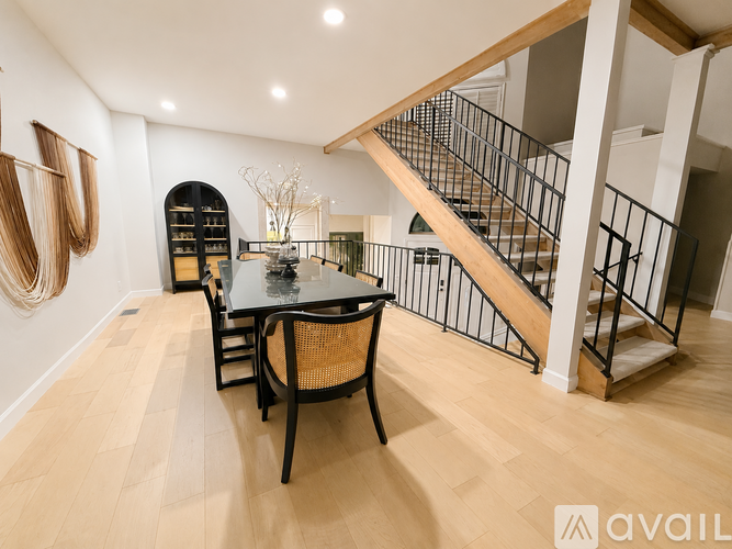 A dining room with a black table and chairs and a staircase in the background.