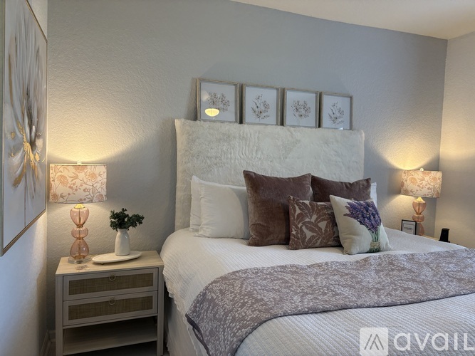 A bedroom with a large bed, a nightstand with a plant, and framed pictures on the wall.