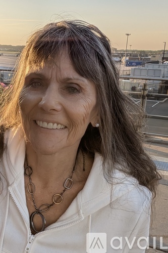 A woman with a white jacket and a necklace is smiling.