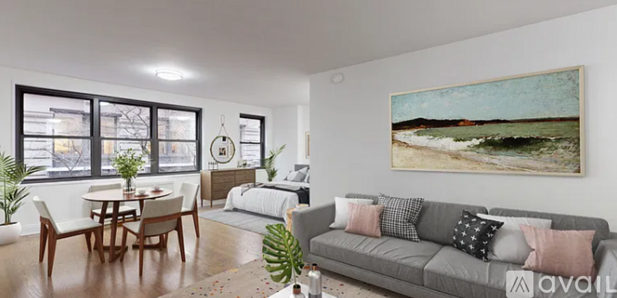 A living room with a grey couch, a dining table with chairs, a bed with a white comforter, and a painting on the wall.