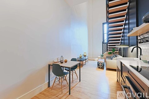 A modern kitchen with a dining table and chairs in the foreground and a staircase in the background.