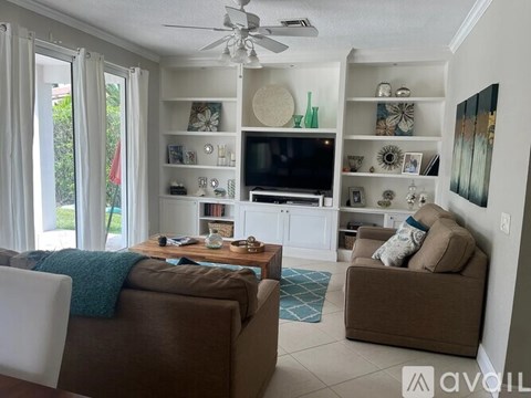 A living room with a brown couch, a white chair, and a television on a white cabinet.