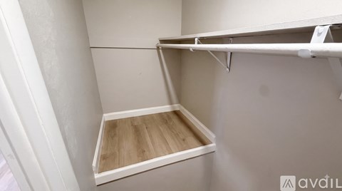 A white closet with a shelf and a wooden floor.