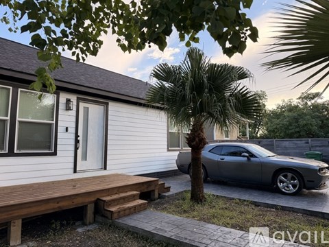 A car is parked in front of a house with a wooden deck and a palm tree.