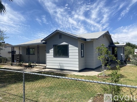A house with a grey roof and white walls is surrounded by a chain link fence.
