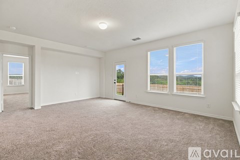 A spacious room with carpeted floor, two windows, and a door leading to a balcony.