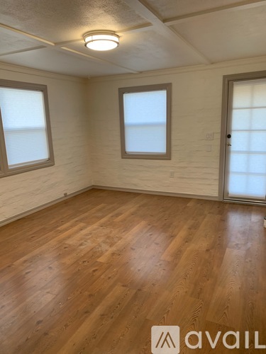 A room with wooden flooring and two windows.