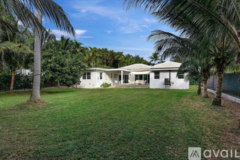 A white house with a lawn and palm trees in front.