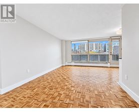 A room with wooden flooring and a view of a city skyline through the windows.