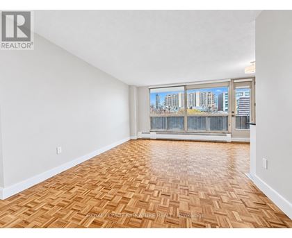 A room with wooden flooring and a view of a city skyline through the windows.