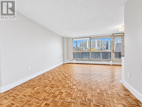 A room with wooden flooring and a view of a city skyline through the windows.