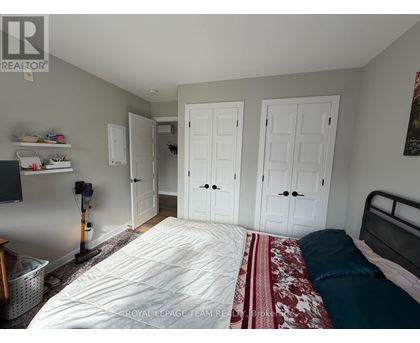 A bedroom with a bed, two closets, and a vacuum cleaner.