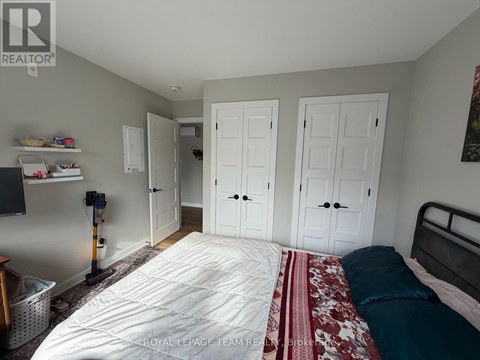 A bedroom with a bed, two closets, and a vacuum cleaner.