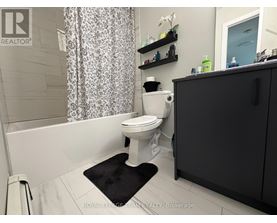 A white toilet in a bathroom with a black mat in front of it.