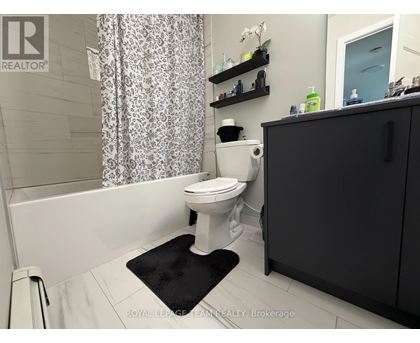 A white toilet in a bathroom with a black mat in front of it.